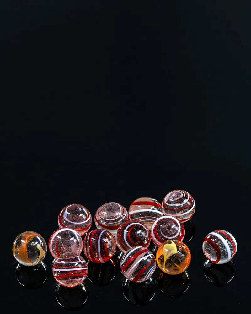 Várias contas de vidro redondas, em tons de vermelho, laranja e branco com riscas em espiral, sobre fundo escuro